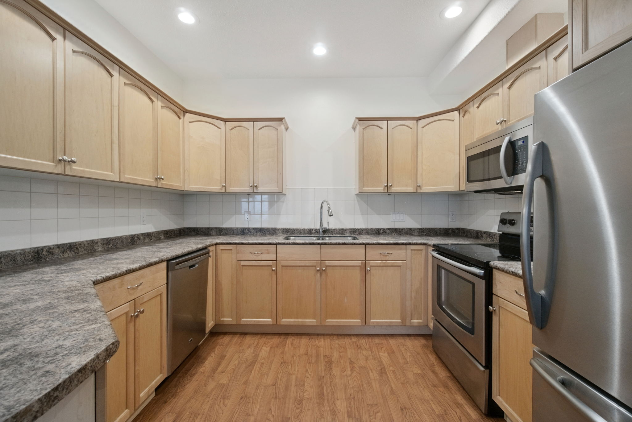 The kitchen with maple cabinetry, a stainless steel refrigerator, range and dishwasher, and a microwave hood fan under recessed lighting.